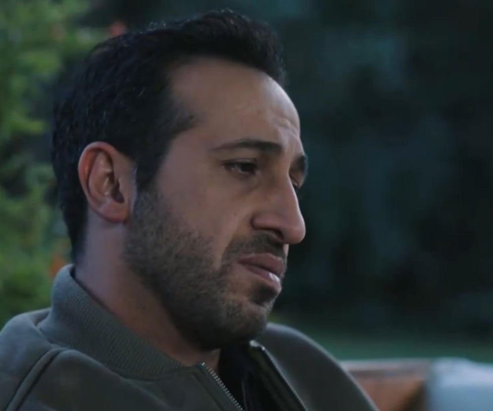 Abidin, postać z serialu „Złoty chłopak”, z brodą i krótkimi, ciemnymi włosami, ubrany w zieloną kurtkę, z wyrazem zamyślenia lub smutku na twarzy, w tle rozmazana zieleń. Aktor Ersin Arıcı w roli Abidina, na Super Seriale można przeczytać o jego dążeniu do prawdy.