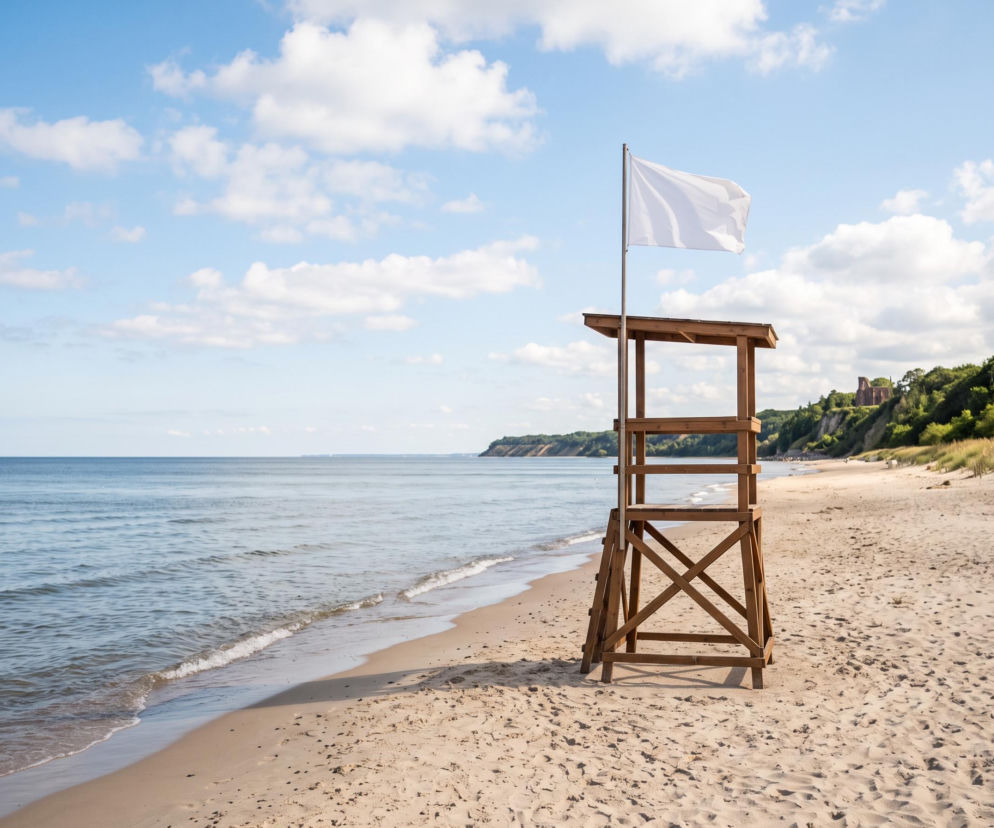 Drewniana wieża ratownicza z białą flagą na pustej plaży w Trzęsaczu. O bezpieczeństwie kąpieli przeczytasz w SE Szczecin.