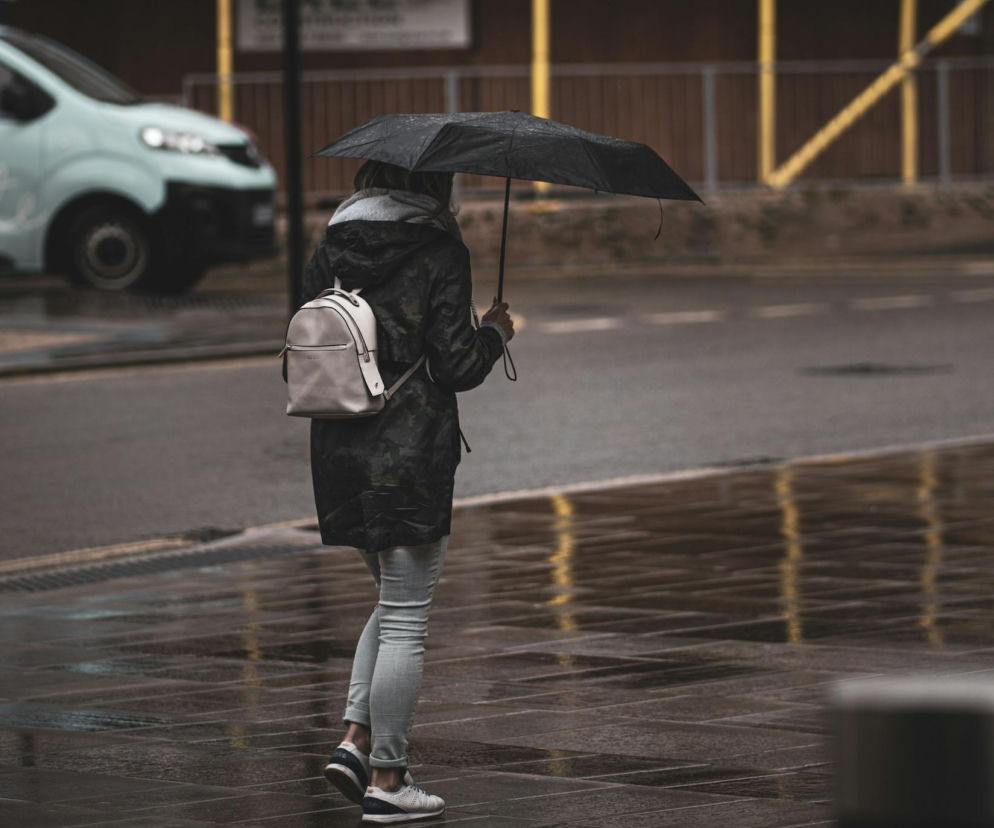 Kobieta z czarnym parasolem idzie przez miasto w deszczowy dzień. O jesiennej pogodzie przeczytasz na SE Pogoda.