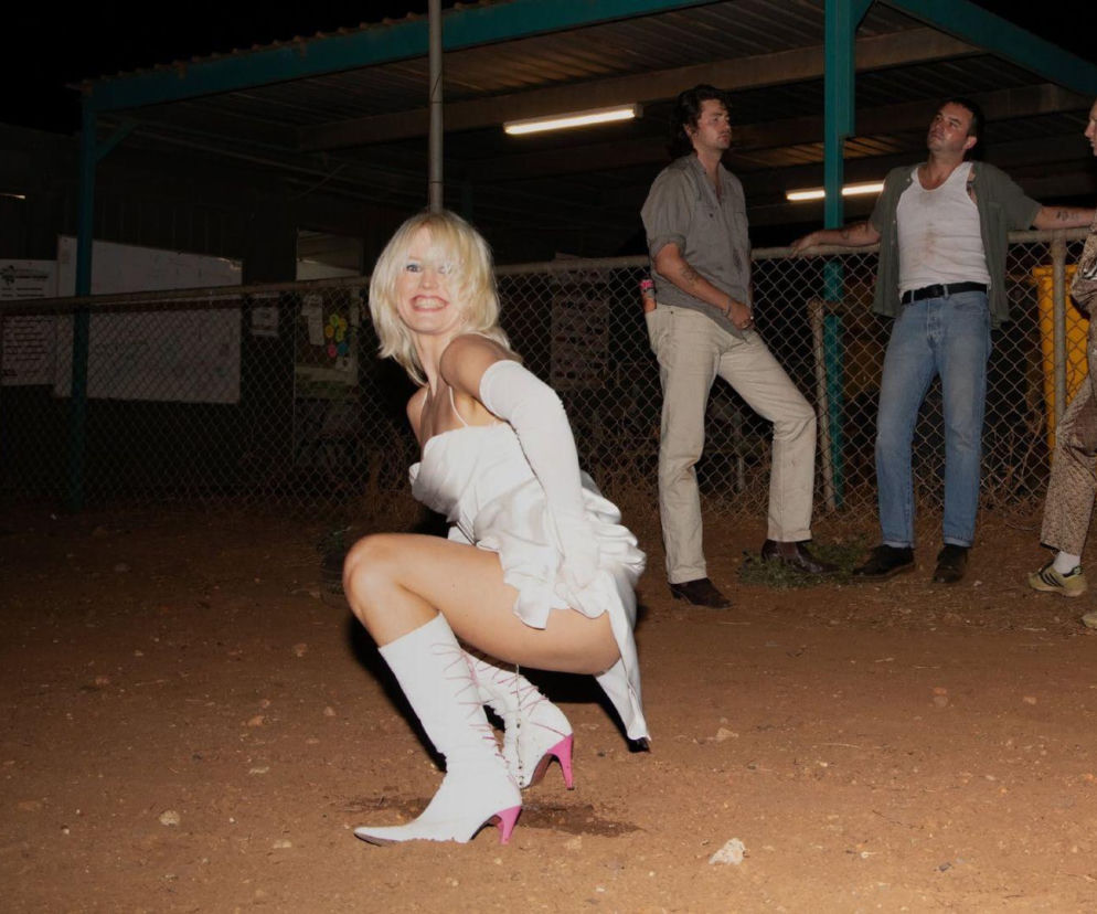 Zespół Amyl and The Sniffers na zewnątrz. Wokalistka kuca w białej sukni. O nowym albumie przeczytasz na EskaRock.