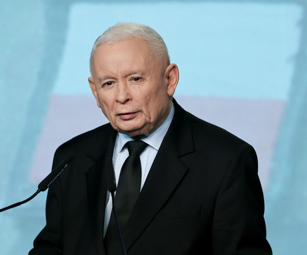 Jarosław Kaczyński, prezes PiS, przemawia podczas konferencji, ubrany w elegancki czarny garnitur i krawat. W tle widoczny jest jasnoniebieski ekran. Więcej informacji o karierze politycznej Kaczyńskiego znajdziesz na naszym portalu.