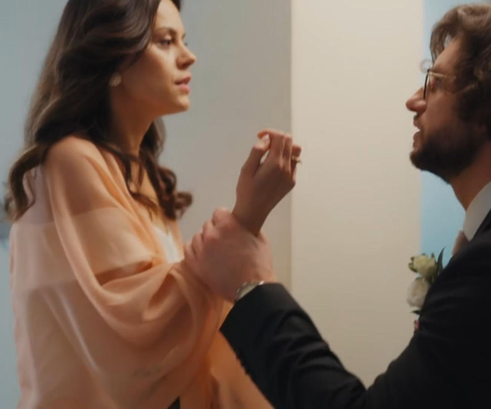 Kasia (Paulina Lasota) i Mariusz (Mateusz Mosiewicz) z M jak miłość. Mariusz, w garniturze ślubnym z przypiętą białą różą, szarpie Kasię za rękę. Kobieta ubrana w lekką, jasnoróżową bluzkę z szerokimi rękawami, patrzy na niego z wyraźnym zdenerwowaniem. Kadr oddaje napięcie przedślubne. Więcej o ich losach na Super Seriale.