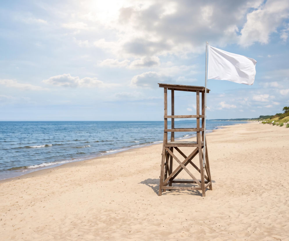 Drewniana wieża ratownicza z białą flagą na pustej plaży w Trzęsaczu. O warunkach kąpieli przeczytasz na SE Szczecin.