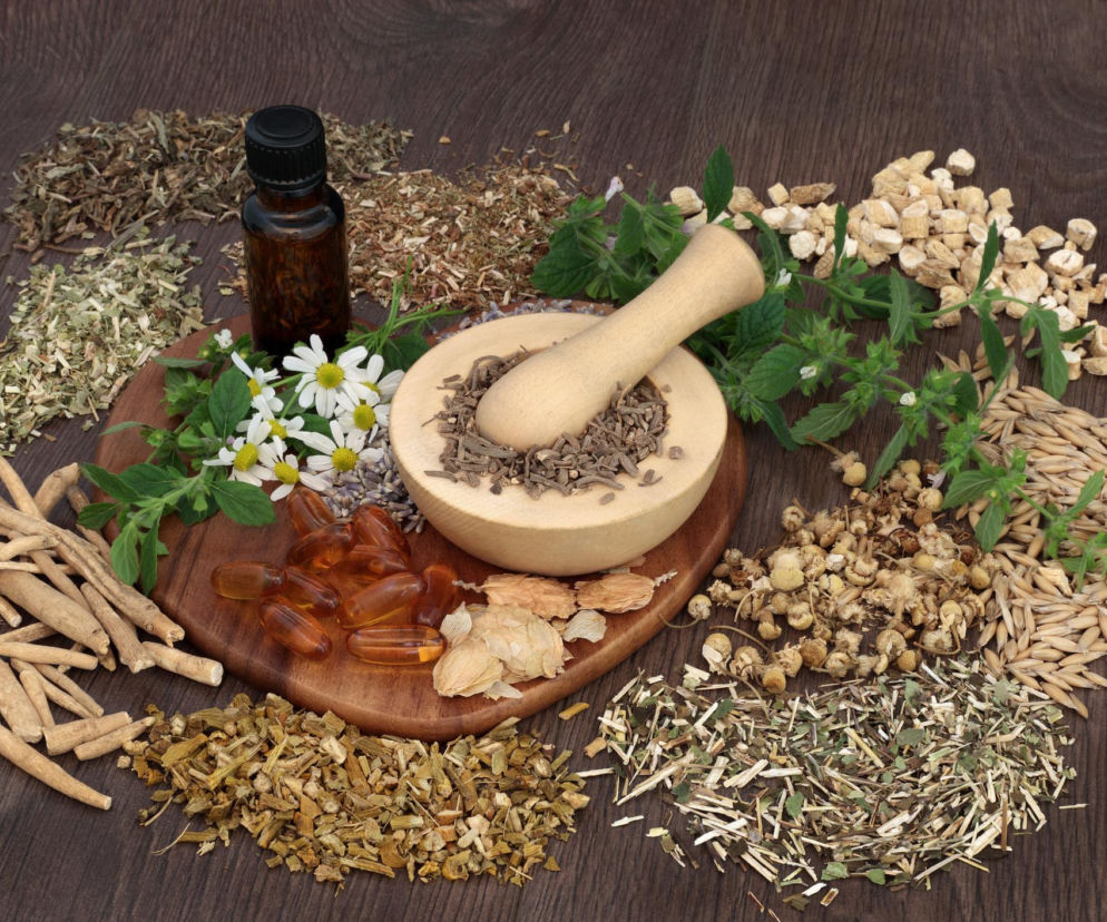 Mieszanka suszonych ziół, korzeni kozłka lekarskiego, rumianku, ashwagandhy, chmielu i passiflory, kapsułki oraz buteleczka z olejkiem eterycznym na drewnianej tacy. Zioła mogą wspierać sen, o czym więcej przeczytasz na Poradnik Zdrowie.