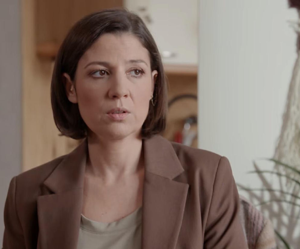 Kinga (Aleksandra Zienkiewicz) z serialu Pierwsza miłość, zaniepokojona zniknięciem Artura, spogląda w dal, ubrana w beżową marynarkę. Scena podkreśla emocje związane z poszukiwaniami i dramatyczne wątki, o których można przeczytać na Super Seriale.