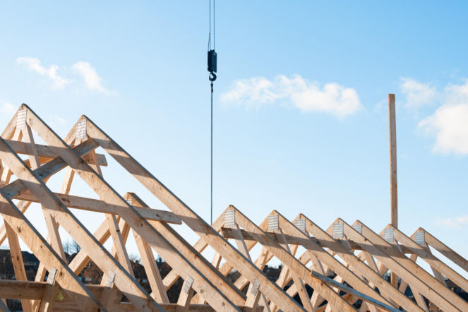 Drewniana więźba dachowa z hakiem dźwigu na tle błękitnego nieba.