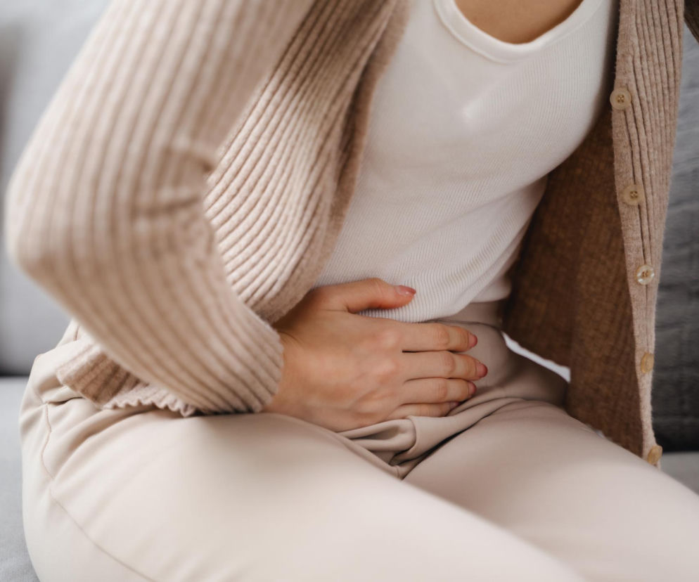 Siedząca kobieta trzyma się ręką za bolący brzuch. O związku endometriozy z cukrzycą przeczytasz na Poradnik Zdrowie.