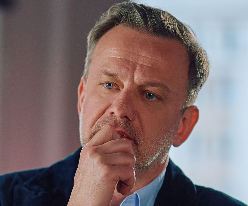 Zamyślony Krzysztof Smolny z serialu Na Wspólnej trzyma dłoń przy ustach. O jego śledztwie przeczytasz na Eska.