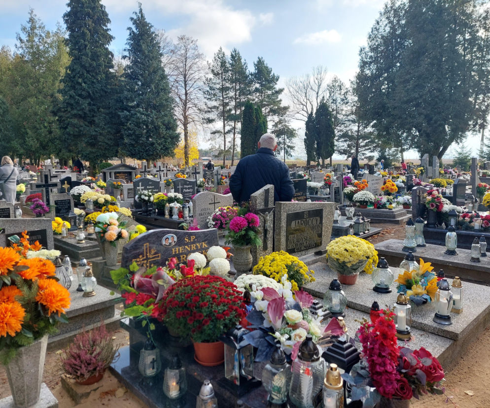 Mężczyzna tyłem na cmentarzu pełnym zniczy i chryzantem. O wolnym za 1 listopada przeczytasz na SE.