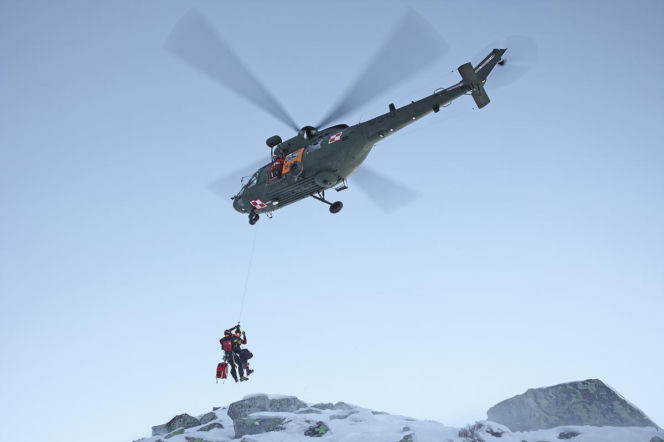 Ratownik górski opuszczający się na linie z helikoptera nad ośnieżonym szczytem. O akcji w Tatrach przeczytasz na SE.
