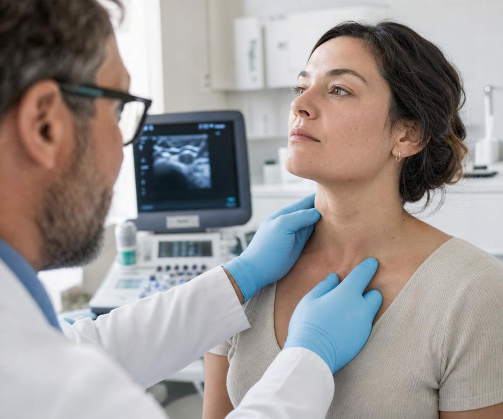 Lekarz w rękawiczkach bada szyję pacjentki. W tle monitor USG. O diagnozowaniu guzów przeczytasz na Poradnik Zdrowie.
