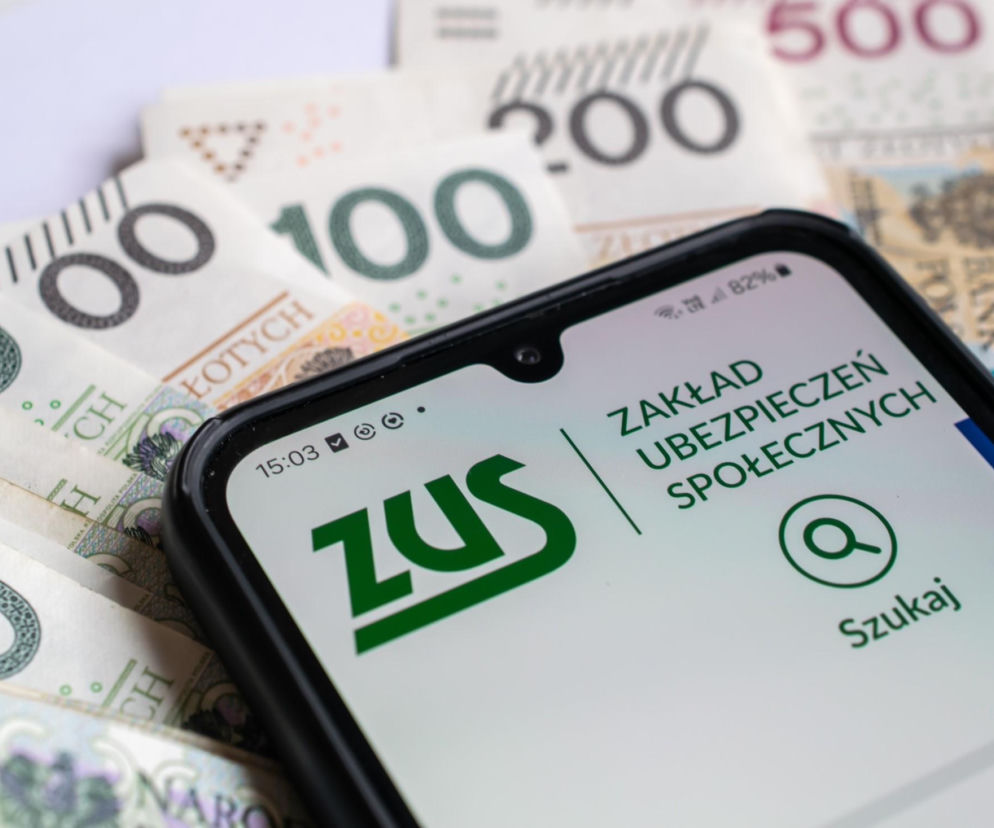 Smartfon z otwartą aplikacją ZUS, leżący na stosie banknotów 100, 200 i 500 złotych, symbolizujący wysokie składki ZUS. Artykuł na Super Biznes informuje o wzroście opłat dla przedsiębiorców, których termin płatności za marzec upływa 20 kwietnia.
